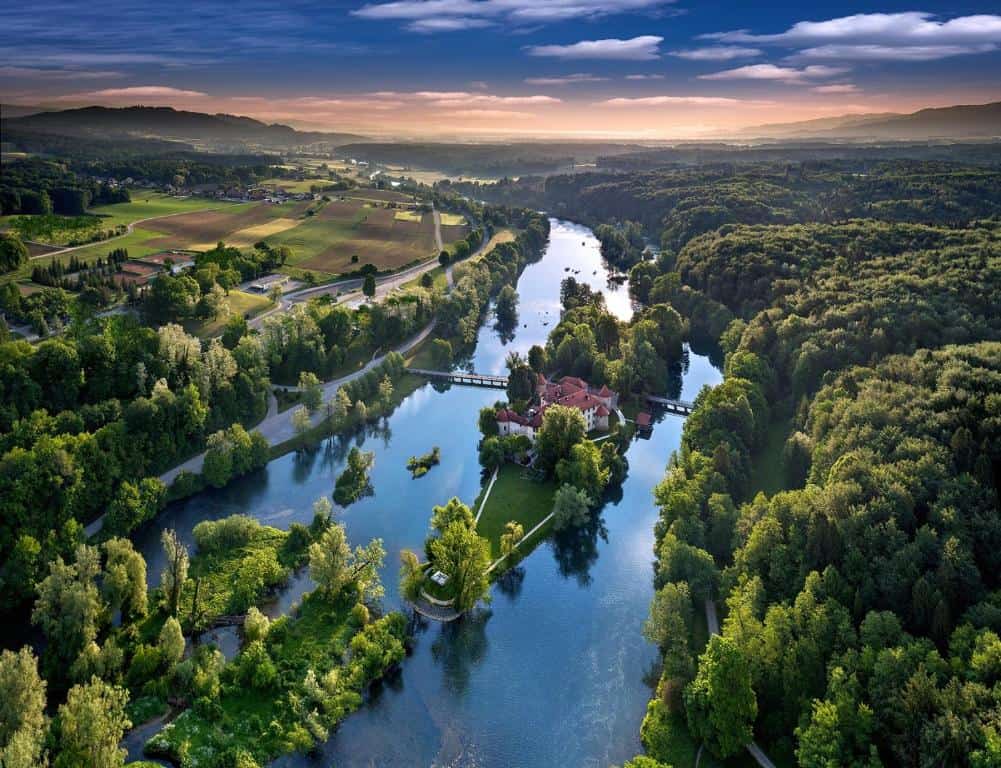 Best luxury hotels Slovenia. Grad Otočec Castle Hotel at sunrise, surrounded by river and forest, Slovenia’s most iconic luxury retreat