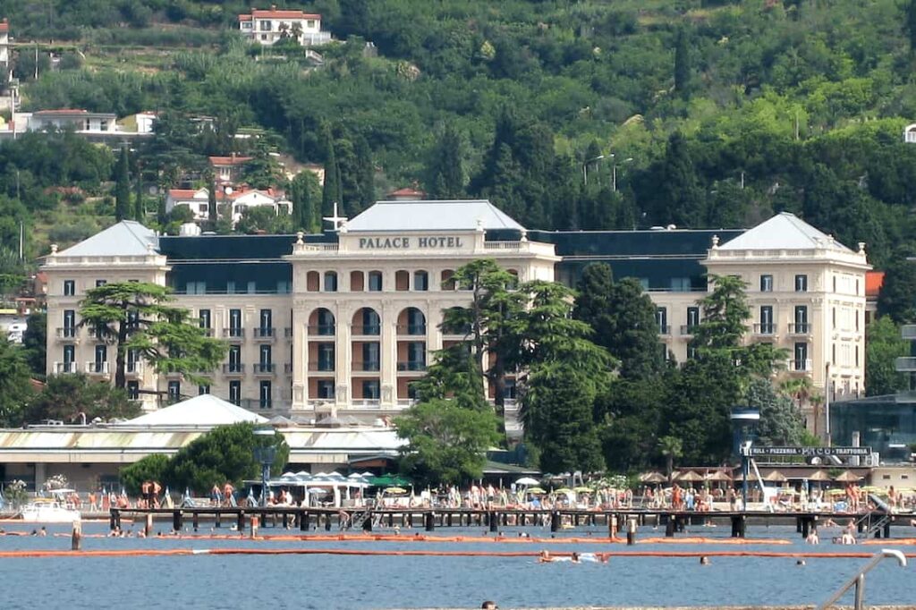 Slovenia’s Most Exclusive luxury hotel Kempinski Palace Portorož with Belle Époque architecture, palm trees, and Adriatic Sea view at sunset.