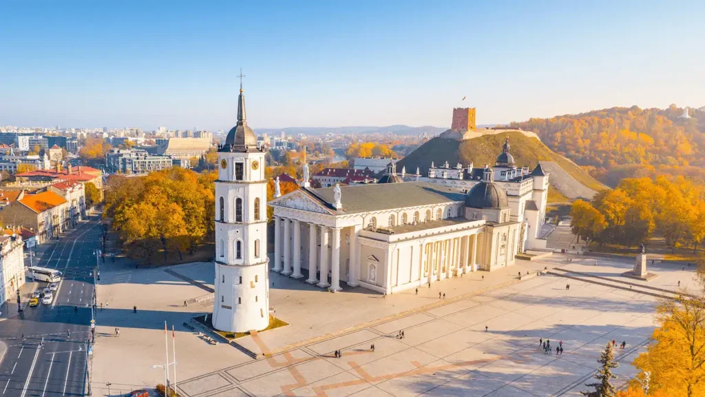 An audit of best historic hotels in Lithuania: A panoramic hero view featuring the red-brick Gediminas' Tower on the castle hill and the Neoclassical Vilnius Cathedral with its standalone Bell Tower.