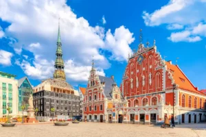 An audit of best historic hotels in Latvia: Panoramic view of Riga Town Hall Square featuring the ornate Dutch Renaissance facade of the House of the Blackheads and the Gothic spire of St. Peter’s Church.