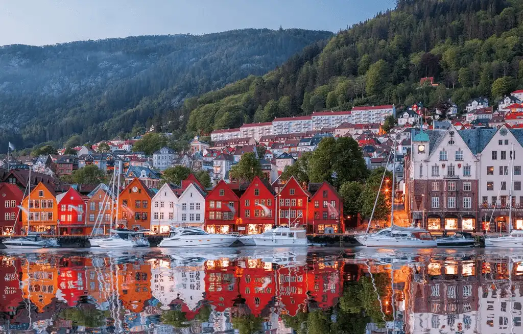 A row of iconic, colorful wooden Hanseatic warehouses at Bryggen in Bergen, Norway, reflecting in the water at twilight—representing the best historic hotels in Norway and their absolute historical assets.