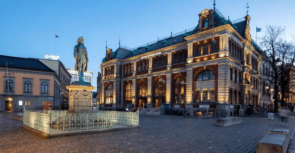The monumental 1862 Neo-Renaissance facade of Bergen Børs Hotel, formerly the city's stock exchange, illuminated at dusk with the Ludvig Holberg statue in the foreground—a definitive landmark among the best hotels in Bergen.