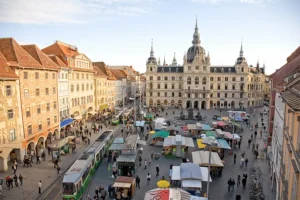 A panoramic view of the Graz Hauptplatz featuring the Town Hall and the Schlossberg fortress in the background, anchoring the best hotels in Graz historic audit.
