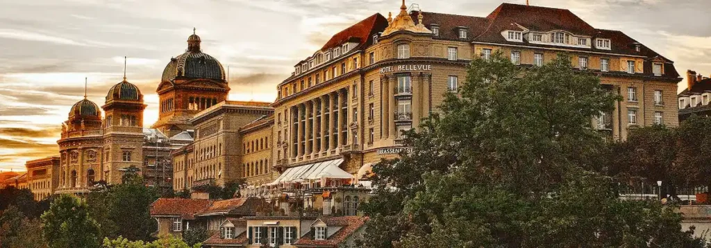 The landmark 1913 neoclassical facade of Bellevue Palace standing directly adjacent to the Swiss Federal Palace, the most recognizable historical anchor in Switzerland and one of the best hotels in Bern.