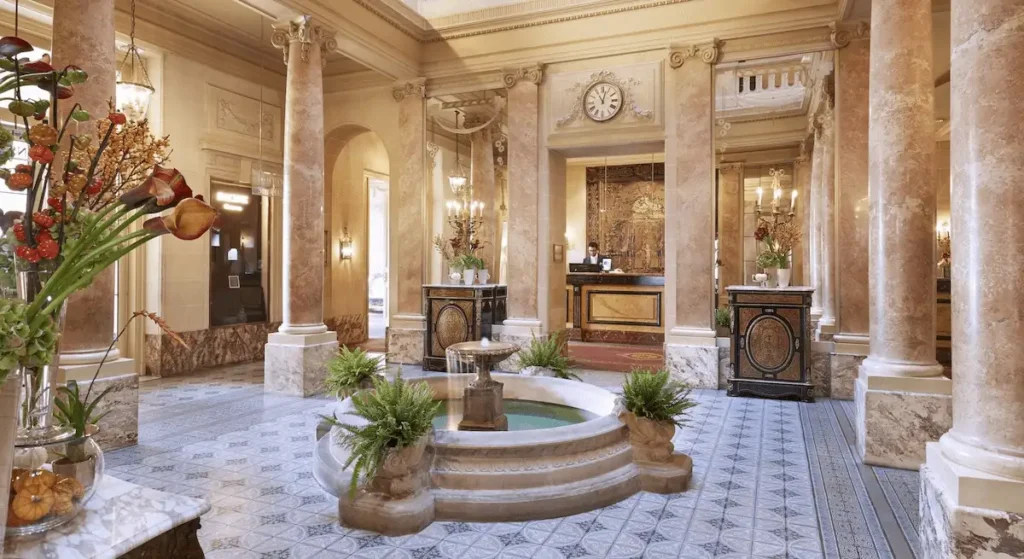 The historic 19th-century Pompeian-style atrium lobby and central fountain of Beau-Rivage Genève, the iconic 1865 site where the birth of the Czechoslovak Republic was signed and one of the best hotels in Geneva.