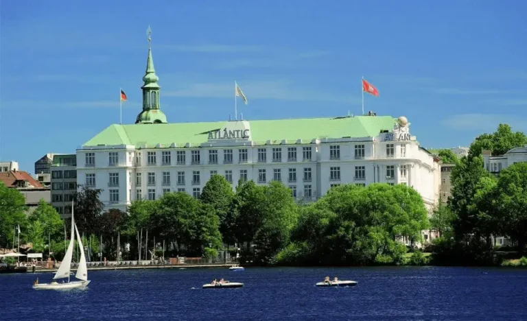 A panoramic view from the Outer Alster Lake of the gleaming white facade and green patina roof of Hotel Atlantic Hamburg, the city’s most recognizable maritime landmark and the best hotels in Hamburg.
