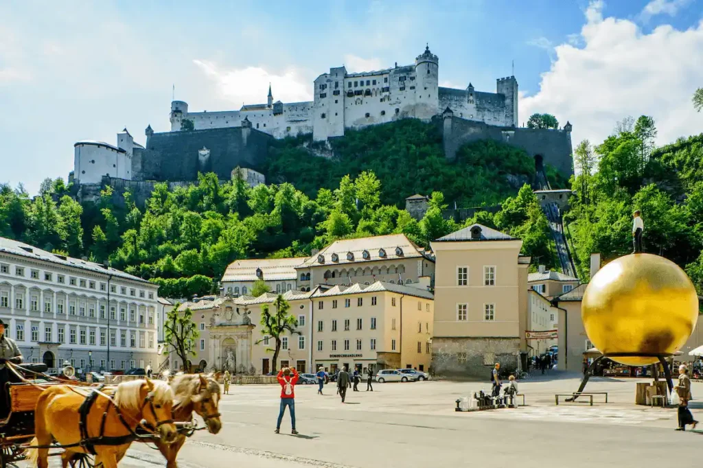 The Hohensalzburg Fortress and Sphaera sculpture at Kapitelplatz, a central landmark for travelers visiting the best hotels in Salzburg.
