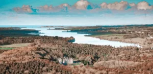 An expansive aerial view of Belleek Castle nestled within dense forestry along the banks of the River Moy estuary, illustrating the property's isolated territorial command in County Mayo.