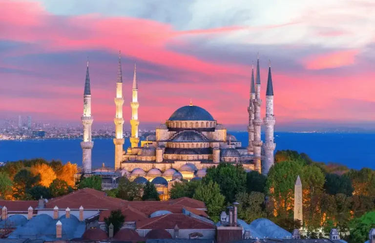 A panoramic sunset view of the 17th-century Blue Mosque (Sultan Ahmed Mosque) and the Sea of Marmara as seen from a heritage terrace, representing the historic skyline surroundings of the best hotels in Istanbul.