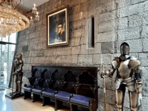 The interior of Clontarf Castle Hotel featuring original stone walls with defensive arrow-loop windows, suits of plate armour, and a carved wooden settle.
