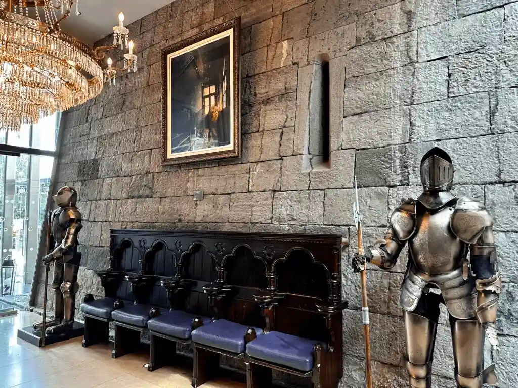 The interior of Clontarf Castle Hotel featuring original stone walls with defensive arrow-loop windows, suits of plate armour, and a carved wooden settle.