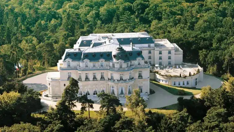 Aerial view of the Neoclassical stone facade and manicured grounds of InterContinental Chantilly Château Mont Royal, positioned as a private forest estate within the Chantilly region.