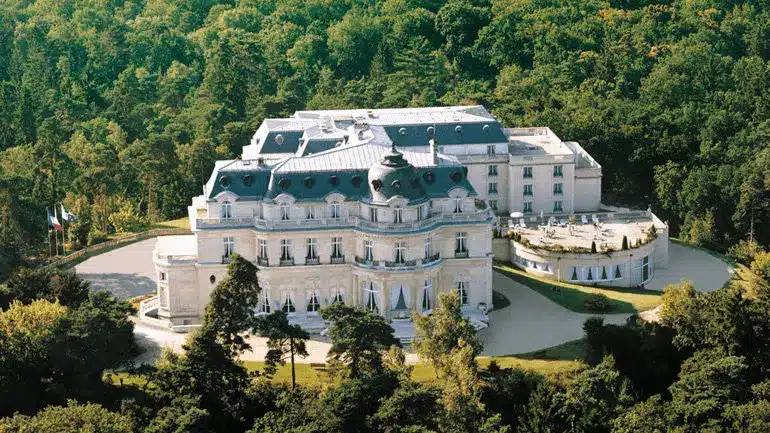 Aerial view of the Neoclassical stone facade and manicured grounds of InterContinental Chantilly Château Mont Royal, positioned as a private forest estate within the Chantilly region.