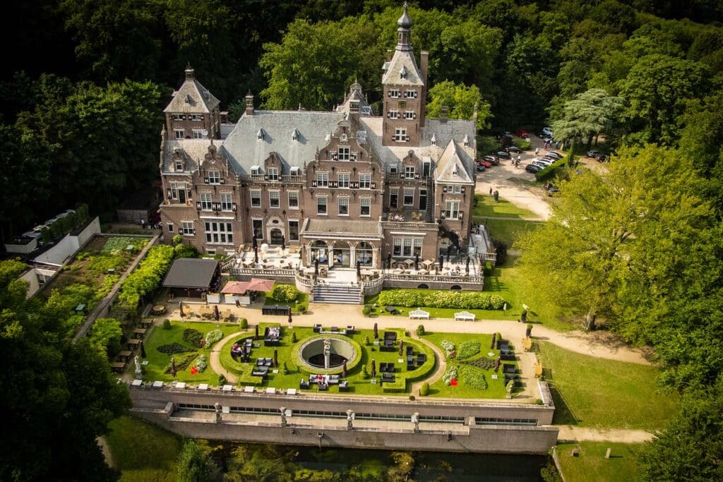 The symmetrical red-brick and stone Classical Revival facade of Landgoed Duin & Kruidberg, featuring grand arched windows and a central portico set within the Dutch National Park dunes.