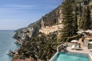 Aerial view of the Anantara Convento di Amalfi Grand Hotel built into the cliffs with its infinity pool overlooking the Amalfi Coast coastline.