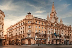 The ornate Italian Renaissance-style facade of Anantara New York Palace Budapest, featuring the landmark clock tower and intricate stone carvings against a soft sunset sky.