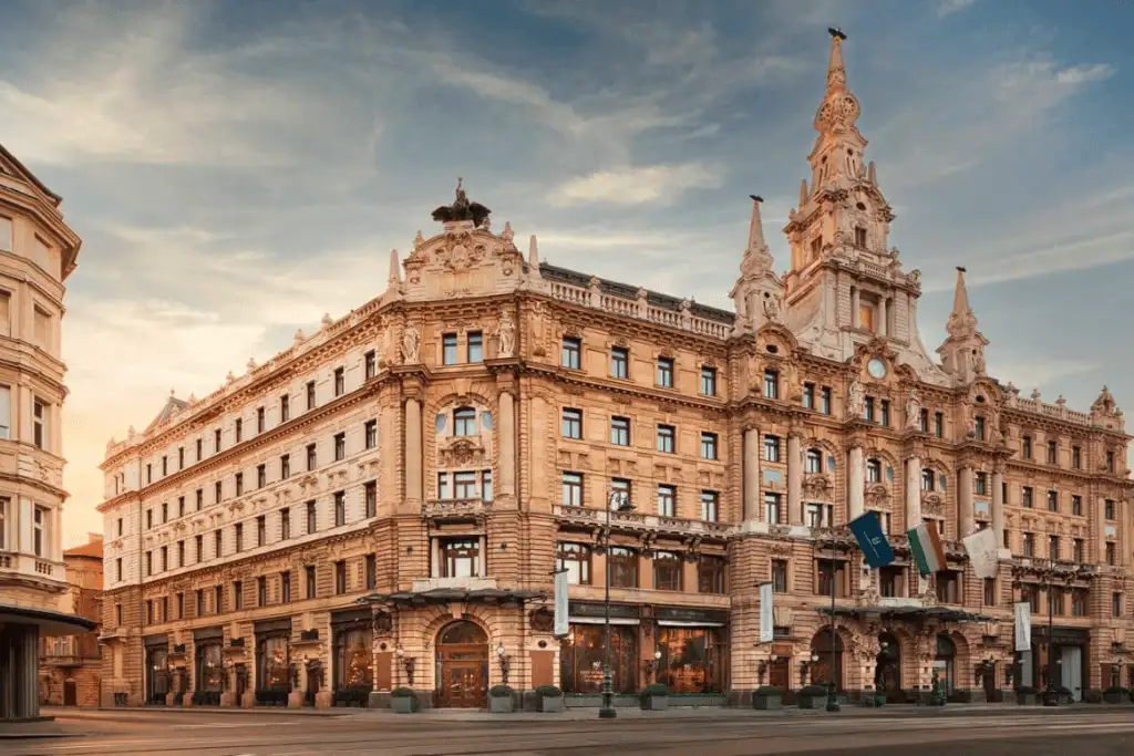 The ornate Italian Renaissance-style facade of Anantara New York Palace Budapest, featuring the landmark clock tower and intricate stone carvings against a soft sunset sky.