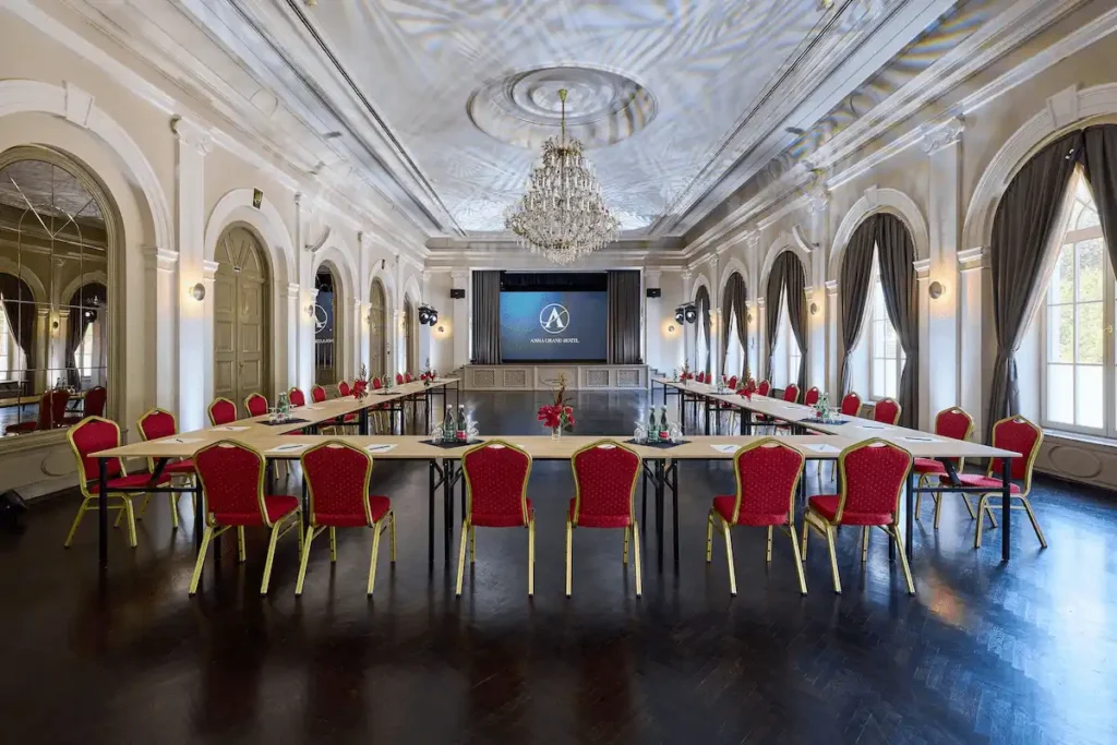 The grand neoclassical ballroom of Anna Grand Hotel in Balatonfüred, featuring high ceilings, ornate stucco work, a large crystal chandelier, and a professional conference setup.