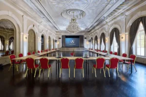 The grand neoclassical ballroom of Anna Grand Hotel in Balatonfüred, featuring high ceilings, ornate stucco work, a large crystal chandelier, and a professional conference setup.