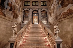 The 1732 "Scalone dei Giganti" (Staircase of the Giants) by Andrea Tirali at Ca' Sagredo Hotel Venice, featuring marble cherub sculptures and expansive 18th-century frescoes.