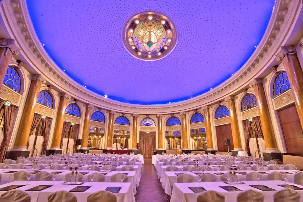 The monumental Emerald Ballroom of Esplanade Zagreb Hotel featuring a soaring blue-lit dome, classical golden columns, and a majestic Art Deco chandelier arranged for a formal event.
