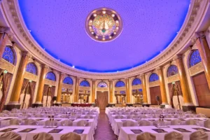 The monumental Emerald Ballroom of Esplanade Zagreb Hotel featuring a soaring blue-lit dome, classical golden columns, and a majestic Art Deco chandelier arranged for a formal event.