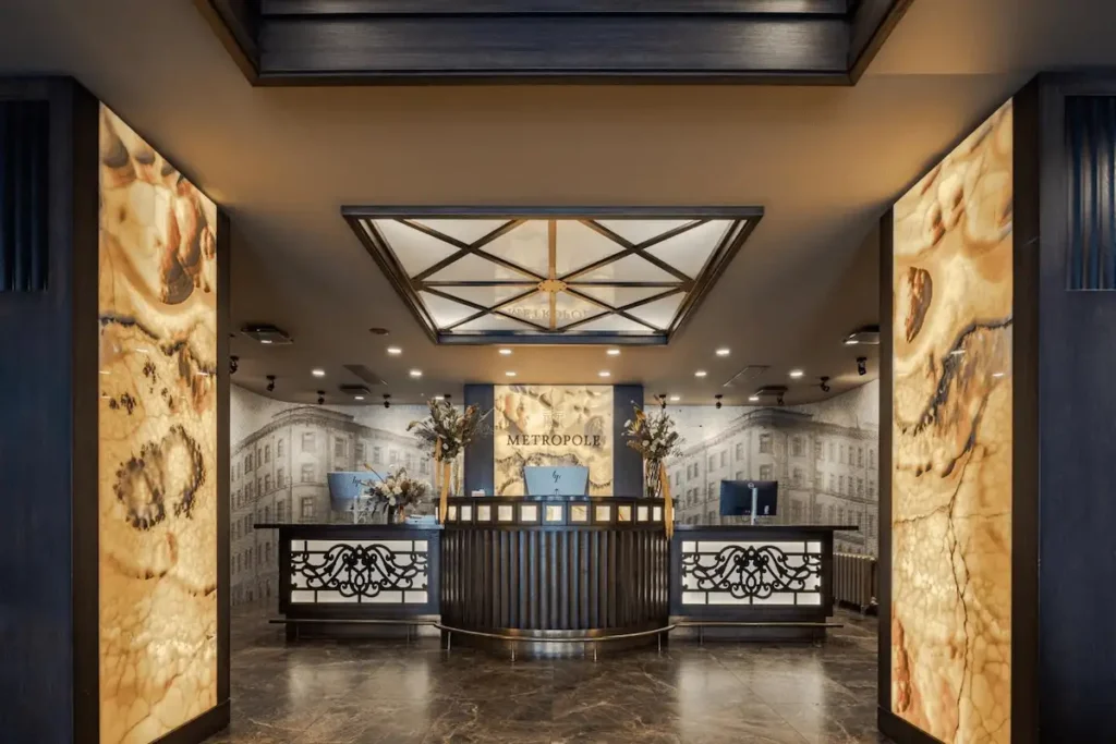 The grand reception area of Eurostars Metropole Riga featuring backlit onyx pillars, dark wood paneling, and a historic mural of the 19th-century facade.