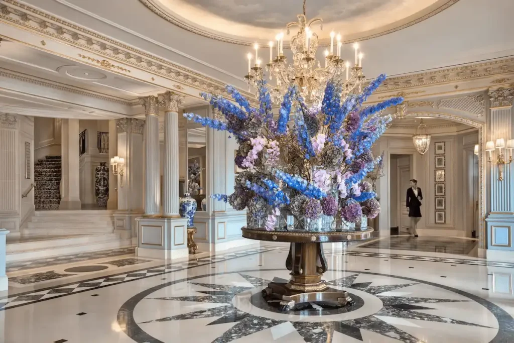 The ornate marble lobby of Four Seasons Hotel des Bergues Geneva featuring a massive, signature floral arrangement beneath a crystal chandelier.