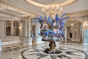 The ornate marble lobby of Four Seasons Hotel des Bergues Geneva featuring a massive, signature floral arrangement beneath a crystal chandelier.