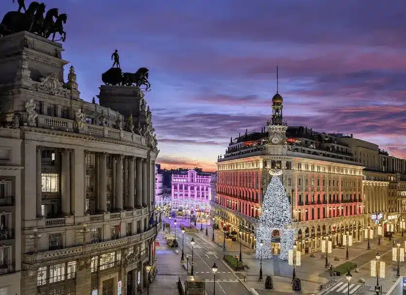 The grand, triangular exterior of Four Seasons Hotel Madrid, showcasing the historic clock tower and copper cupola of the former Palacio de la Equitativa, where the neoclassical architecture of seven heritage buildings meets the vibrant center of Spain's capital.