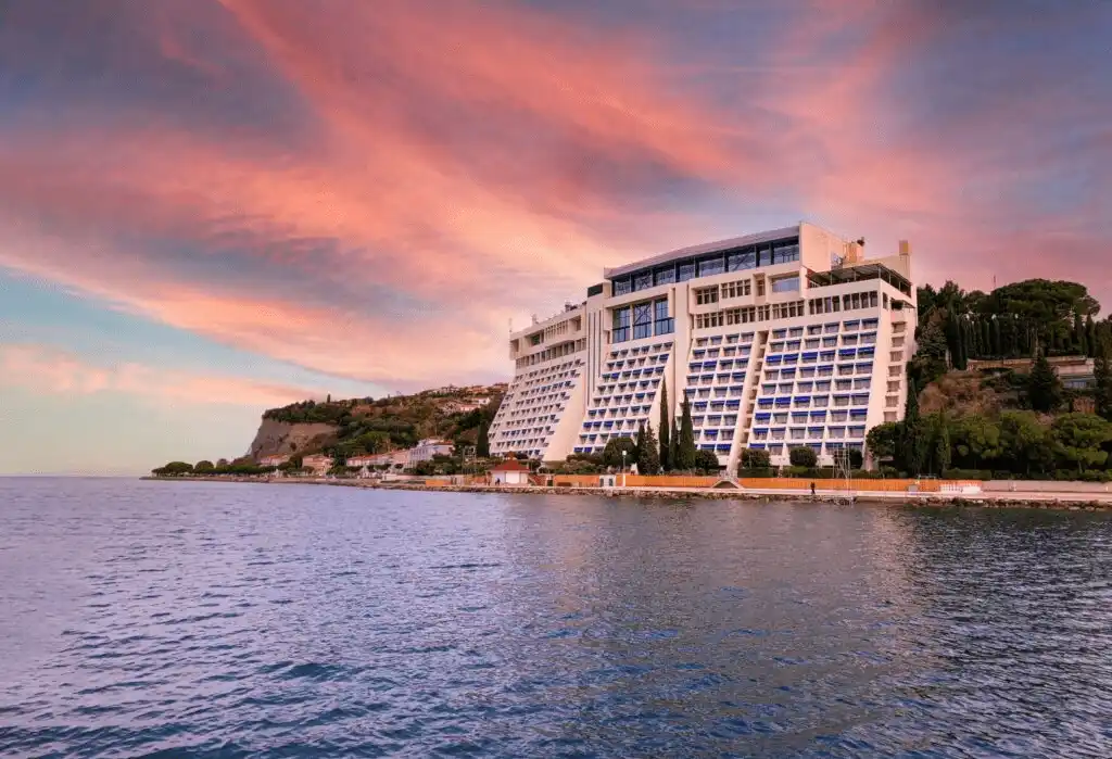The iconic staggered architecture of Grand Hotel Bernardin at sunset, resembling a luxury ocean liner on the cliffs of Portorož with a panoramic view of the Adriatic Sea and the Piran coastline.