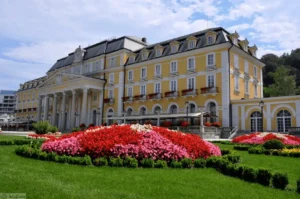 The yellow neo-Baroque facade of Grand Hotel Rogaška featuring classical columns and manicured flower beds in the Rogaška Slatina spa park.