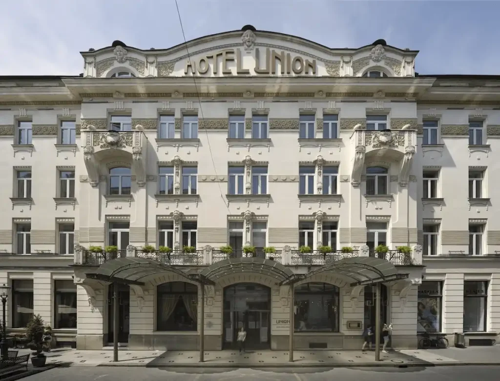 The grand Art Nouveau facade of Grand Hotel Union Eurostars in Ljubljana, featuring ornate stone carvings, classical balconies, and the original 1905 Secessionist glass canopy.