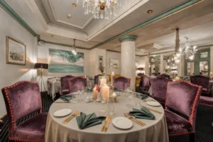 The intimate fine-dining room at Grand Palace Hotel Riga, featuring plush purple velvet chairs, crystal chandeliers, and candlelight set against the historic stone pillars of the former Central Bank.