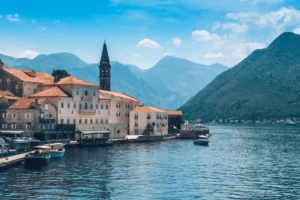 A stunning waterfront view of Heritage Grand Perast in Montenegro, featuring its historic stone palace architecture and bell tower against the backdrop of the Bay of Kotor mountains.