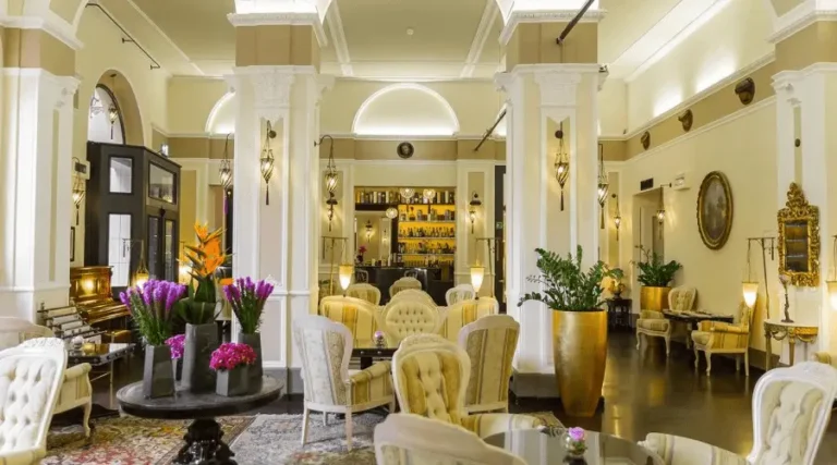 The elegant lobby lounge of Hotel Bernini Palace Florence, featuring cream-colored Neoclassical columns, period armchairs, and sophisticated Moorish-inspired decorative lighting.