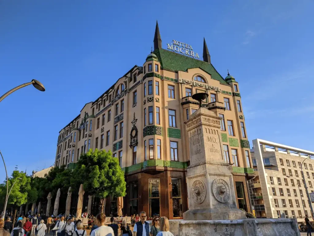 The iconic Russian Secessionist facade of Hotel Moskva in Belgrade, featuring its signature emerald green Zsolnay ceramic tiles and architectural towers under a clear blue sky.