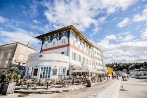 The historic exterior of Hotel Piran, featuring its classical Mediterranean architecture and outdoor cafe on the Piran waterfront.