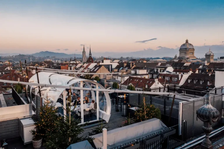 Guests dining inside a transparent Tubbo dome on the Sky Terrace at Hotel Schweizerhof Bern, featuring panoramic winter views of the Bern Old Town and the Federal Palace.