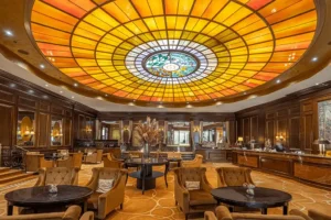 The magnificent 19th-century stained-glass dome in the lobby of Hotel Vier Jahreszeiten Kempinski Munich, featuring intricate designs of the four seasons and bathing "Munich's most beautiful living room" in warm, golden light.