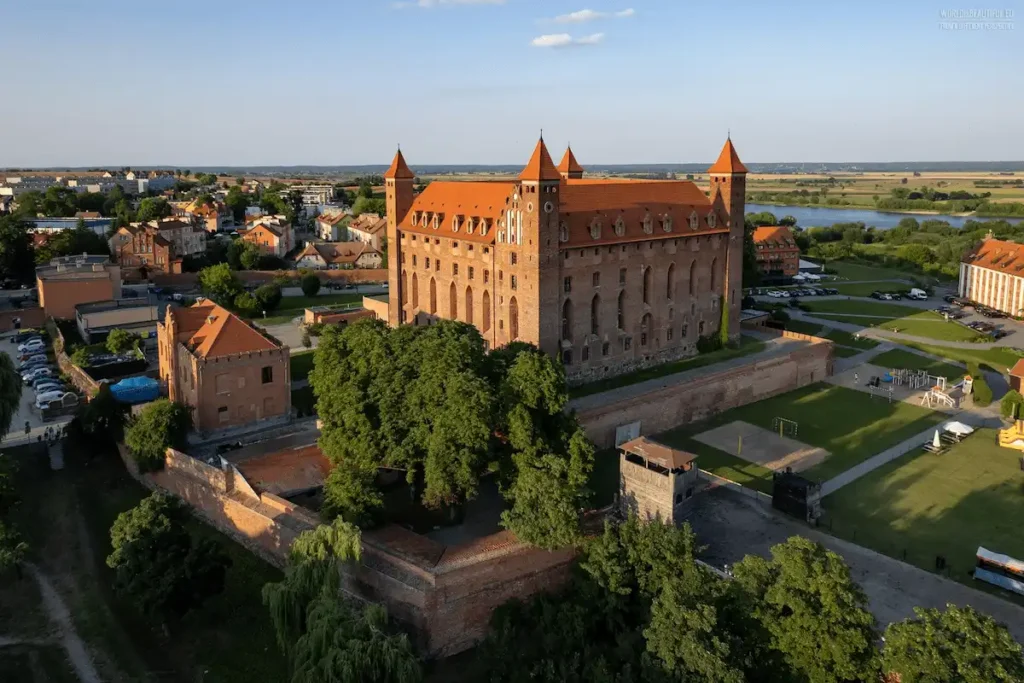 A wide view of Hotel Zamek Gniew, a massive 13th-century Gothic fortress in Pomerania, Poland, featuring its soaring brick walls and four corner towers overlooking the Vistula River valley.