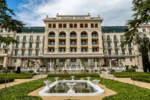 The grand 1910 Austro-Hungarian facade of Kempinski Palace Portorož overlooking a manicured heritage park and stone fountain on the Slovenian coast.