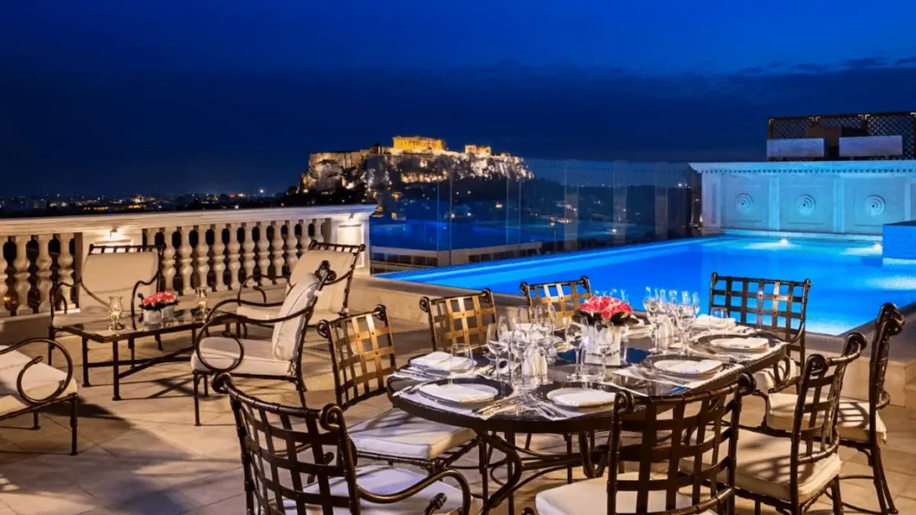 A view from the balcony of the King George hotel in Athens, a historic 1930s landmark that served as a former prime ministerial residence, featuring its neoclassical design and a private penthouse pool overlooking the Acropolis and Parthenon.