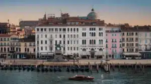 The white 100-window facade of the Londra Palace Venezia on the Riva degli Schiavoni waterfront with the San Marco Basin in the foreground.