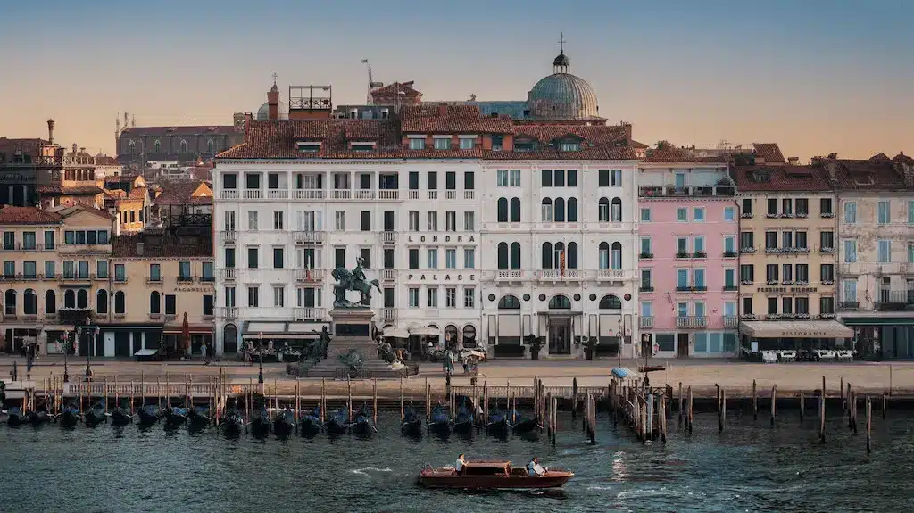 The white 100-window facade of the Londra Palace Venezia on the Riva degli Schiavoni waterfront with the San Marco Basin in the foreground.