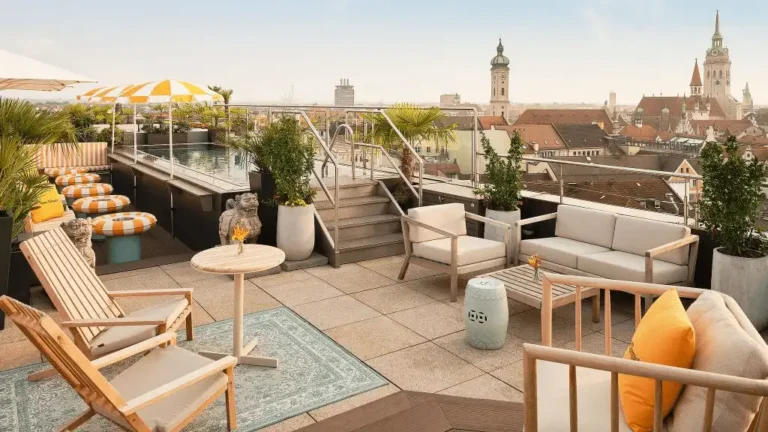 The 7th-floor Mandarin Oriental Munich rooftop terrace featuring a sun-drenched lounge and swimming pool with panoramic views of Munich’s historic red-tiled roofs and the landmark towers of the Frauenkirche.