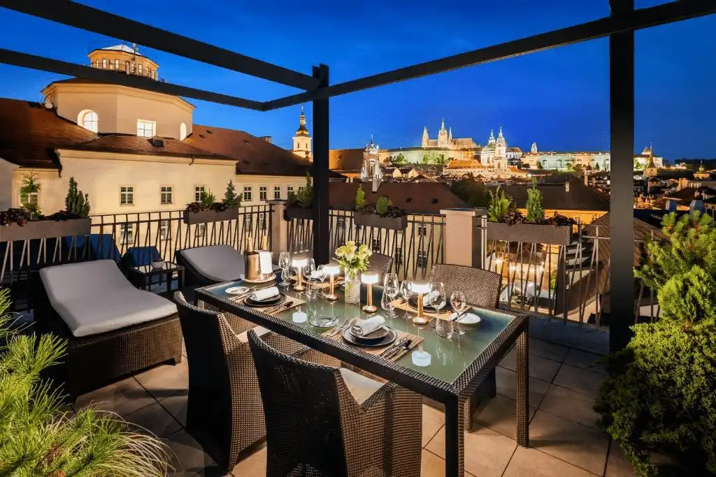 The private rooftop terrace of the Presidential Suite at Mandarin Oriental Prague, featuring a set dining table and panoramic views of Prague Castle and the Malá Strana skyline at twilight.