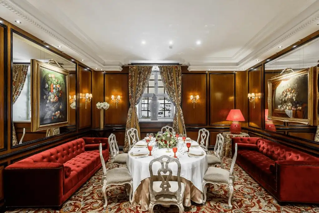 The opulent, wood-paneled "Column Hall" at Narutis Hotel Vilnius, featuring deep red velvet sofas, 18th-century style oil paintings, and an elegant fine-dining table setting.