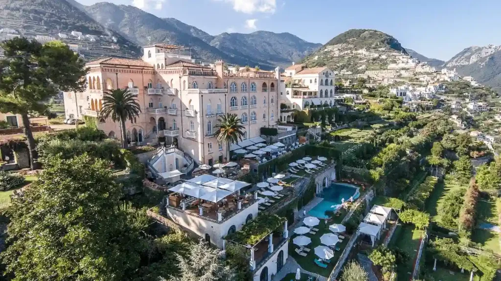 Aerial view of Palazzo Avino, a 5-star hotel in a restored 12th-century pink palace formerly known as Palazzo Sasso, perched 350 meters above the Amalfi Coast in Ravello with terraced gardens and pool.