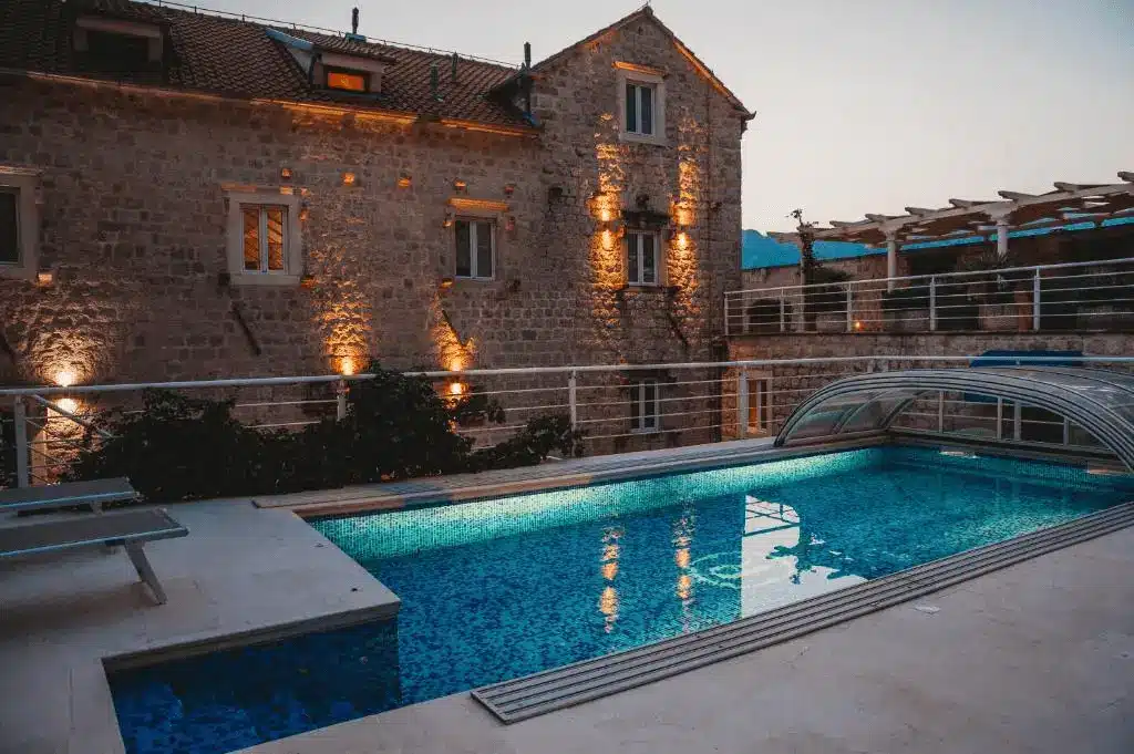 The illuminated outdoor swimming pool of Palazzo Radomiri Heritage Boutique Hotel at dusk, set against the historic stone walls of the 18th-century captain's palace.
